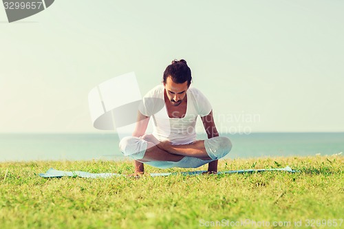 Image of smiling man making yoga exercises outdoors
