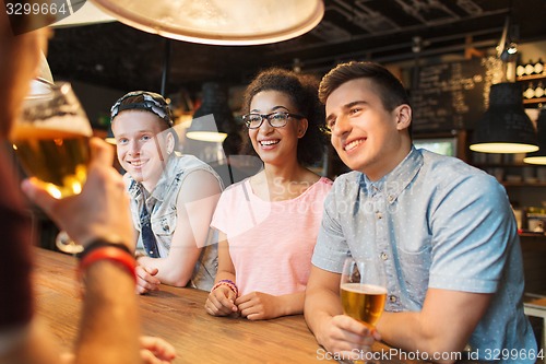 Image of happy friends drinking beer and talking at bar