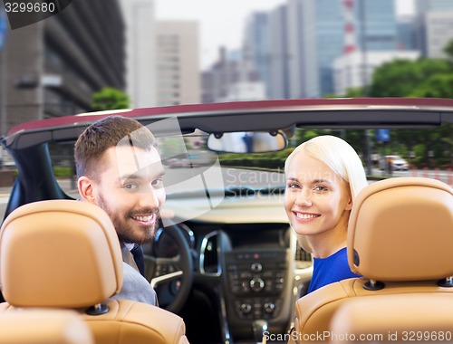 Image of happy couple driving in cabriolet car over city