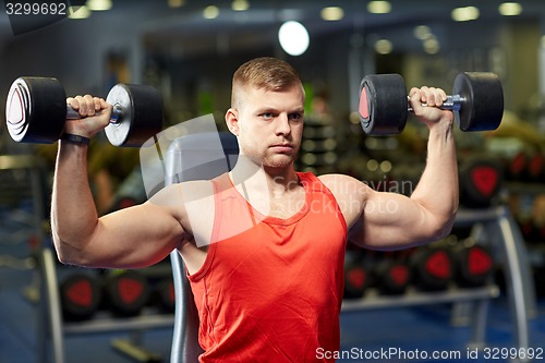 Image of young man with dumbbells flexing muscles in gym