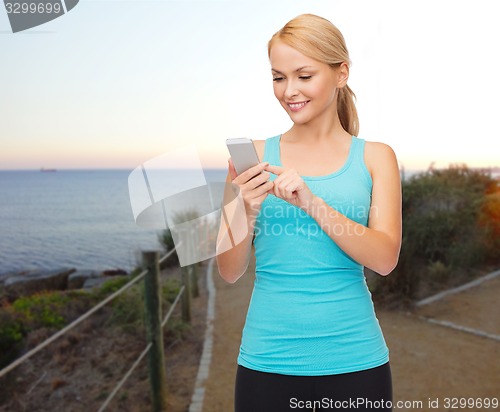 Image of smiling sporty woman with smartphone outdoors