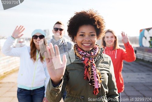 Image of happy teenage friends waving hands on city street