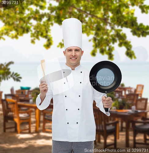 Image of happy male chef holding frying pan and spatula
