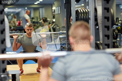 Image of young man flexing muscles with barbell in gym