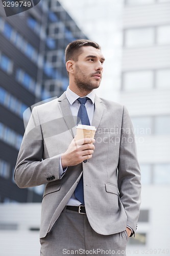 Image of young serious businessman with paper cup outdoors