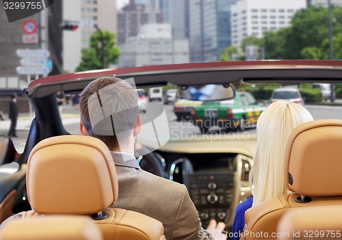 Image of couple driving in cabriolet car over city street