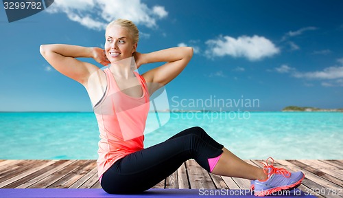 Image of smiling woman doing sit-up on mat over sea