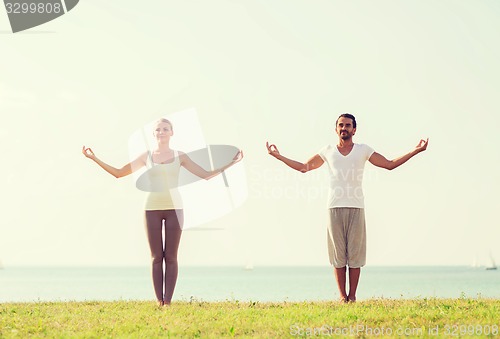 Image of smiling couple making yoga exercises outdoors