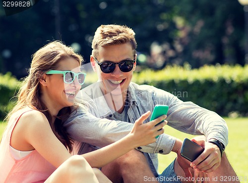 Image of smiling friends with smartphones sitting in park