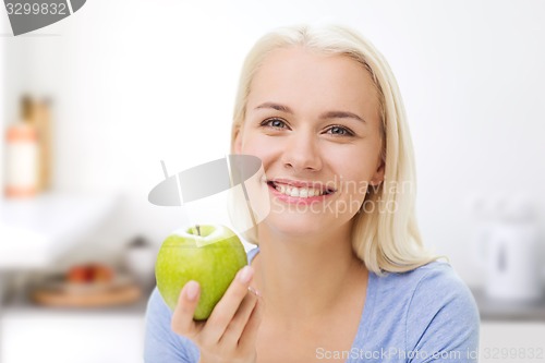 Image of happy woman eating green apple on kitchen