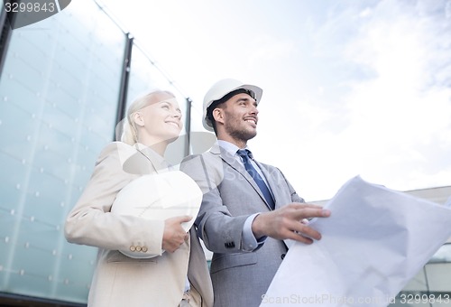 Image of smiling businessmen with blueprint and helmets