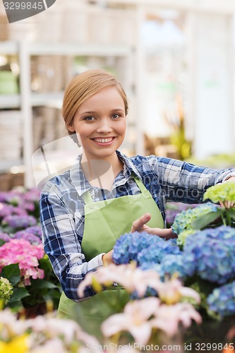 Image of happy woman taking care of flowers in greenhouse