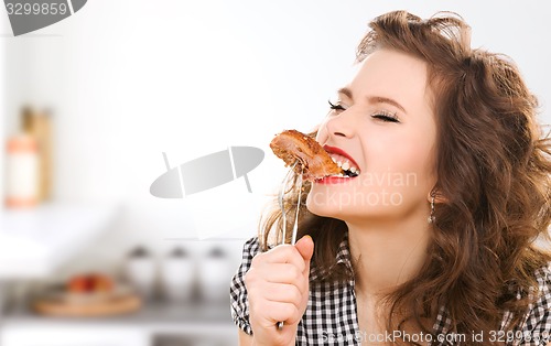 Image of hungry young woman eating meat on fork in kitchen