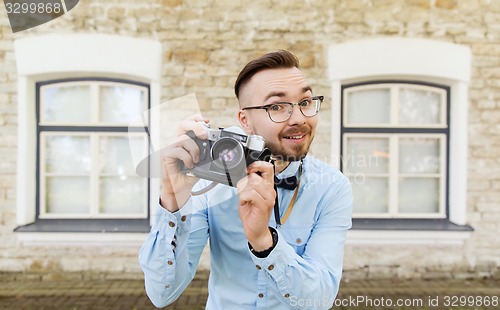 Image of happy young hipster man with film camera in city