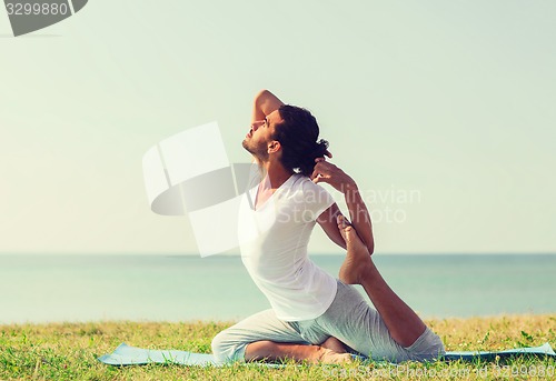 Image of smiling man making yoga exercises outdoors