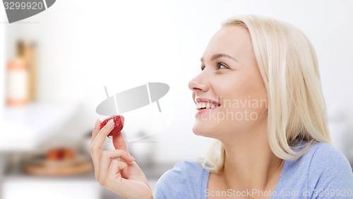 Image of happy woman eating strawberry on kitchen