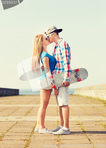 Image of smiling couple with skateboard kissing outdoors