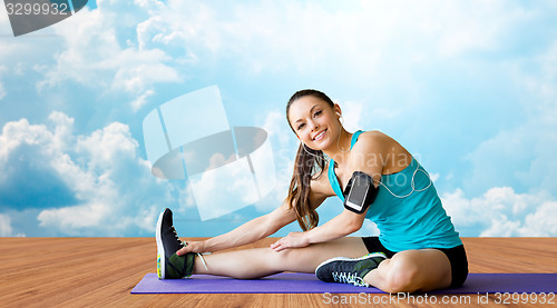 Image of smiling woman stretching leg on mat over clouds