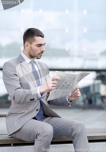 Image of young serious businessman newspaper outdoors