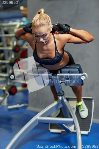 Image of young woman flexing back muscles on bench in gym