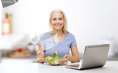Image of smiling woman eating salad with laptop on kitchen