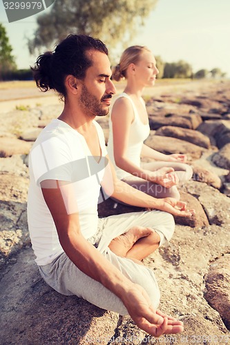 Image of smiling couple making yoga exercises outdoors