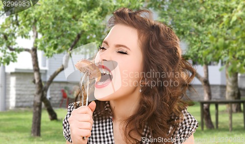 Image of hungry young woman eating meat on fork over house