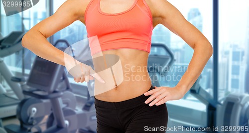 Image of woman pointing finger to her abdomen in gym