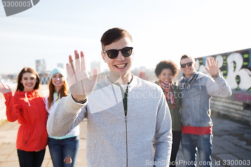 Image of happy teenage friends waving hands on city street