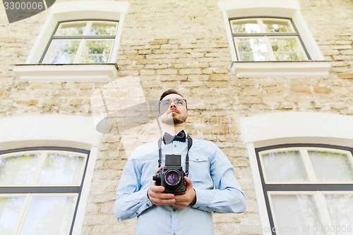 Image of happy young hipster man with film camera in city