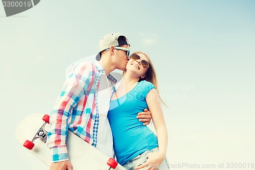 Image of smiling couple with skateboard kissing outdoors