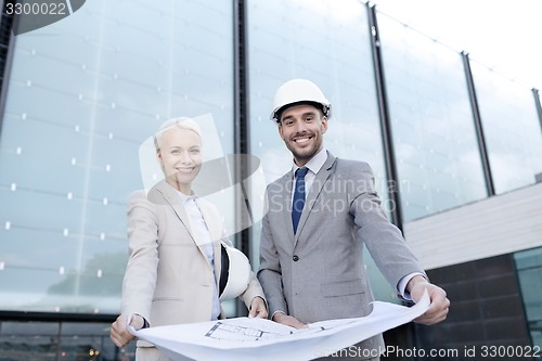 Image of smiling businessmen with blueprint and helmets