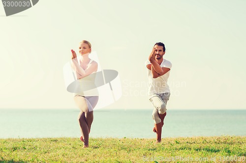 Image of smiling couple making yoga exercises outdoors