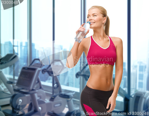 Image of happy woman drinking water from bottle in gym