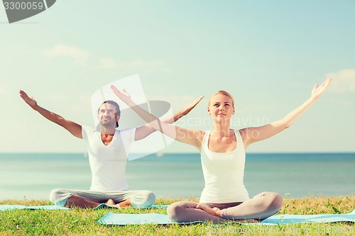 Image of smiling couple making yoga exercises outdoors