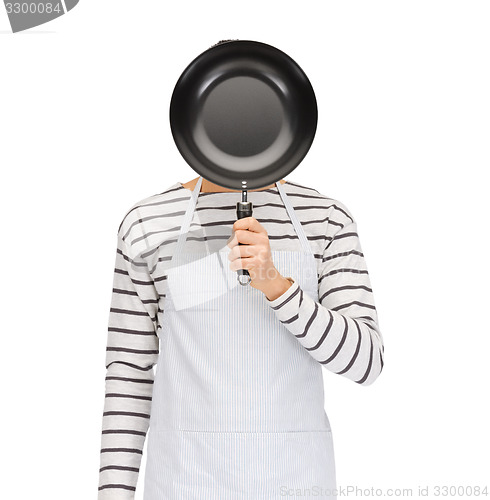 Image of man or cook in apron hiding face behind frying pan