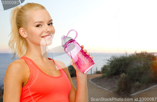 Image of happy woman drinking water from bottle outdoors