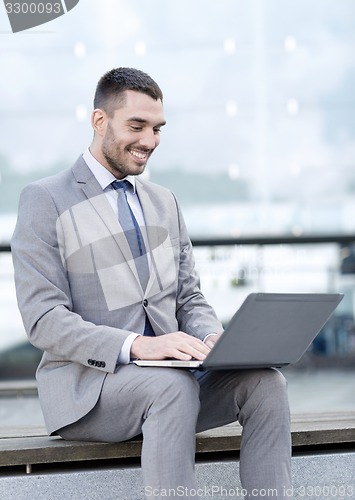 Image of smiling businessman working with laptop outdoors