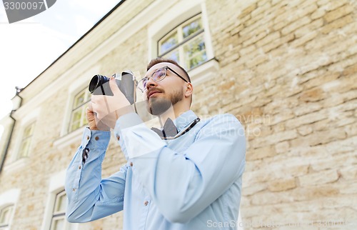 Image of happy young hipster man with film camera in city