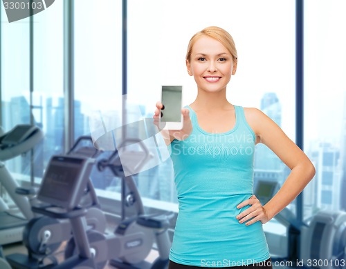 Image of smiling sporty woman showing smartphone in gym