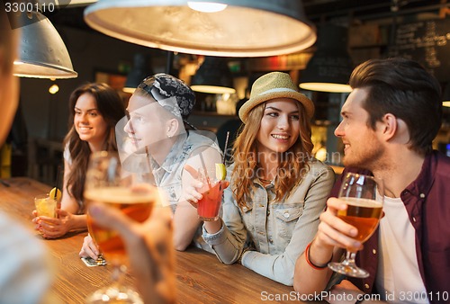 Image of happy friends with drinks talking at bar or pub