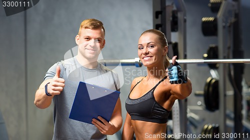 Image of smiling young woman with personal trainer in gym