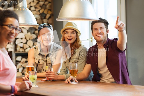 Image of happy friends with drinks pointing finger at bar