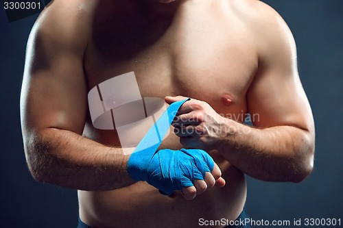 Image of muscular boxer bandaging his hands on gray background