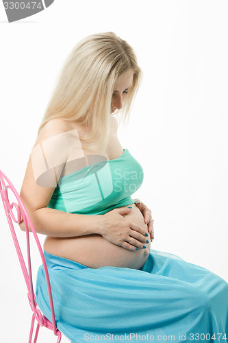 Image of pregnant young woman sitting on a chair and looking at stomach
