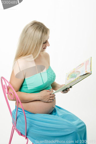 Image of pregnant young woman reading a book sitting on chair