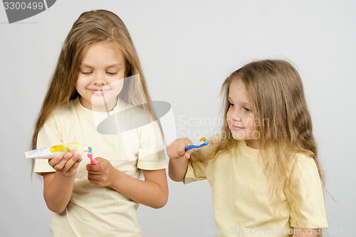 Image of Girl watching sister squeezing toothpaste on the brush