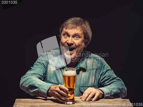 Image of The smiling man in denim shirt with glass of beer