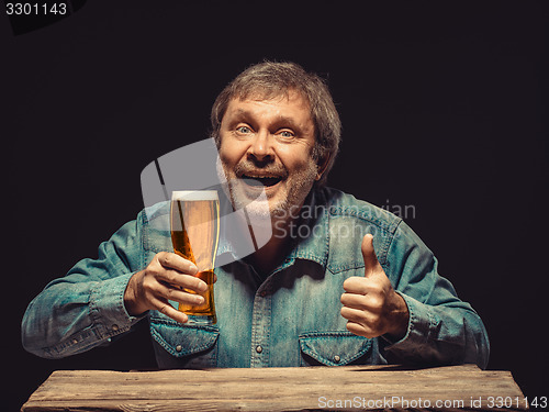 Image of The smiling man in denim shirt with glass of beer