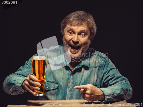 Image of The smiling man in denim shirt with glass of beer